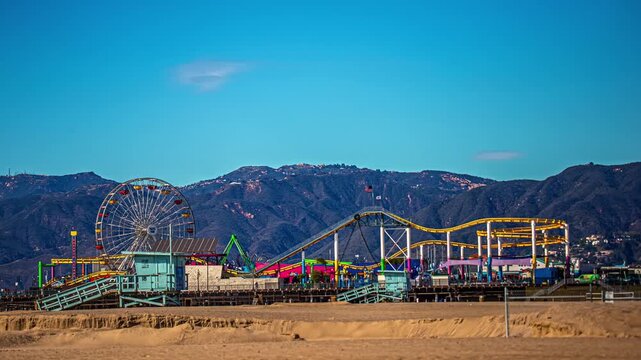 View of Santa Monica Pier featuring the ferris wheel and roller coaster against a mountain backdrop in Los Angeles, California, United States.