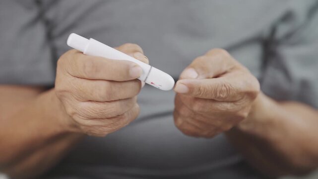 Close up of a senior using a lancing device for fingertip blood sampling before glucose testing, representing diabetes management, blood sugar monitoring, home healthcare, disease prevention.