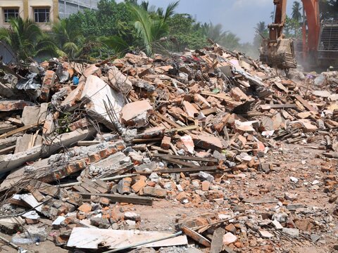 Heavy excavator demolishing a building with rubble and debris on site