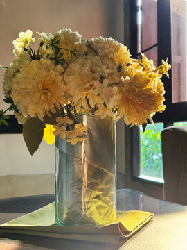 Elegant yellow flower bouquet in a clear glass vase on a table, illuminated by warm sunlight from a window. Perfect for cozy home decor and interior design