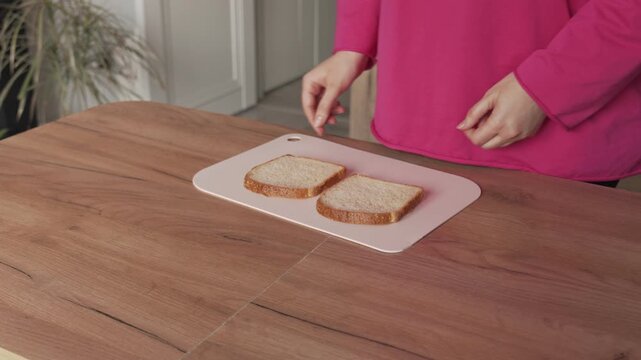 The hands of a housewife woman place pieces of bread on a cutting board on the kitchen table.