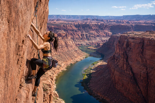 Determined woman fearlessly ascends a majestic sandstone cliff face, showcasing her strength and agility during an exhilarating outdoor rock climbing adventure above a winding river canyon