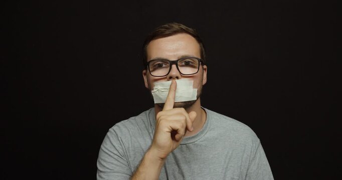 Man with tape over his mouth making a silence gesture. Ideal for censorship, freedom of speech, silence, oppression, and communication concepts.