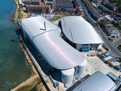 Aerial view of the Woolston Water Treatment Plant with modern curved metal roofs and storage tanks situated along the coastline in Southampton, England, United Kingdom.