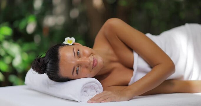 Smiling Woman Resting On Towel At Spa With Frangipani Flower In Her Hair