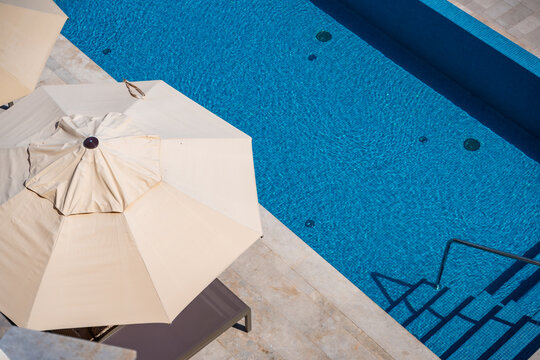 Luxury outdoor swimming pool with sun umbrellas viewed from above at a modern resort. Summer vacation, relaxation and premium hospitality lifestyle.