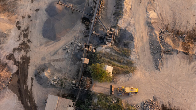 Aerial view of a quarry mining site featuring conveyor belts, piles of gravel, and a yellow loader operating on dusty ground in Klaten, Central Java, Indonesia.