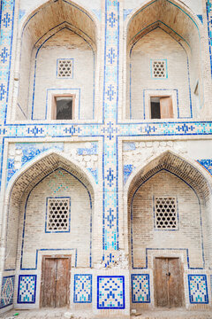 A beautifully preserved section of historic Islamic architecture featuring elegant pointed brick arches, intricate blue mosaic tilework, decorative lattice windows, and weathered wooden doors
