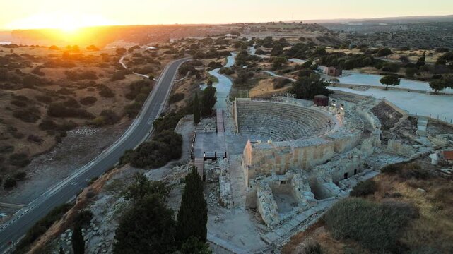 Aerial view of Kourion Ancient Amphitheater in Cyprus at sunset. The historic stone theatre, surrounding ruins and golden evening light create a dramatic archaeological landscape.