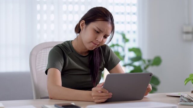 Young Asian woman displaying frustration and bad mood while working on digital tablet at home office