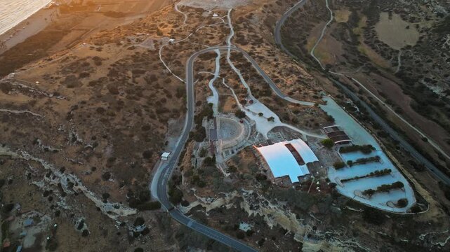 Wide sunset drone view of the Kourion Ancient Amphitheater and its surrounding landscape, presenting the site in a dramatic golden-hour atmosphere.