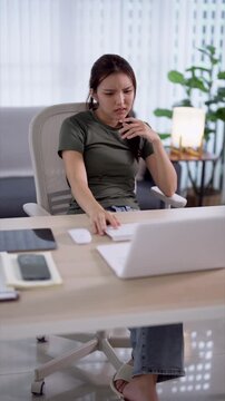 Young Asian woman looking frustrated and thoughtful while working on laptop in modern home office with copy space
