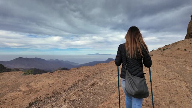 Woman with trekking poles walking on a mountain path. Stunning panoramic view of the mountains of Gran Canaria