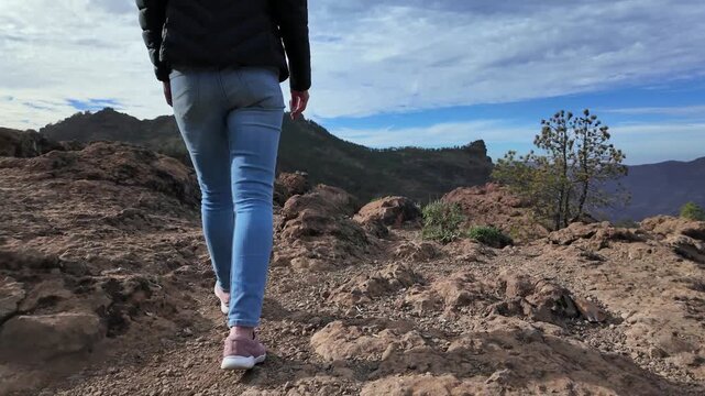 Follow shot of a woman's legs walking on a trail. Scenic volcanic mountain landscape and Roque Nublo, Gran Canaria, Canary Islands