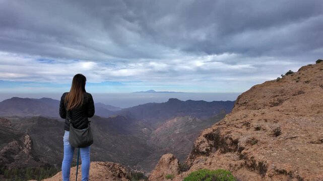 Woman standing on a mountain peak, enjoying the panoramic view of the valley from the Roque Nublo in Gran Canaria, Canary Islands