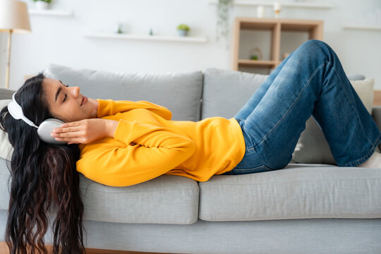 Portrait of Asian woman relaxing listening audio with headphones sitting on a couch at home