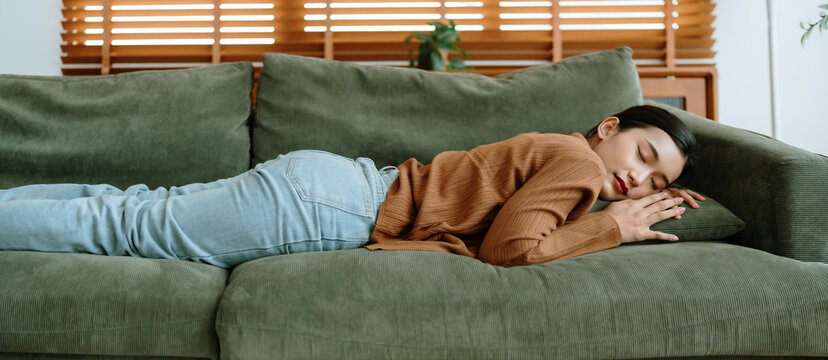 Asian woman resting at home on couch, feeling exhausted after work, lacking energy, or overworked, too tired, and lacking motivation