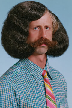 people of ai, yearbook photo of a person with huge dark-brown side-parted bob, stern frown and handlebar mustache, blue check shirt with rainbow tie, photorealistic.png