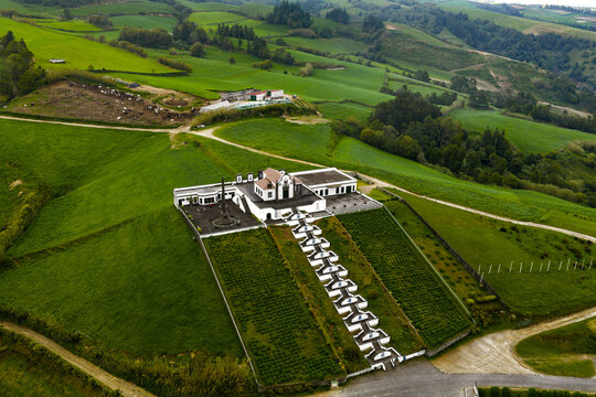 Aerial view of Miradouro da Nossa Senhora da Paz chapel with its iconic staircase, surrounded by lush green hills and rolling agricultural landscapes in Vila Franca do Campo, Azores, Portugal.