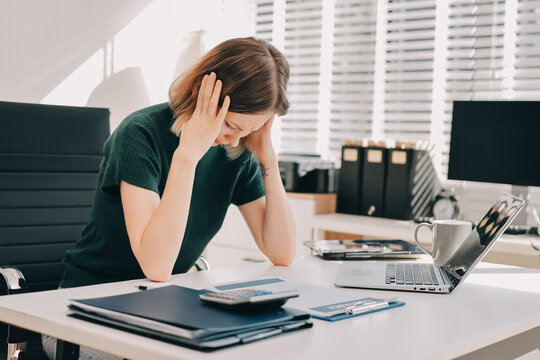 Businesswoman experiencing work related stress and frustration, feeling a headache and burnout from overwhelming tasks while working on her laptop in the office