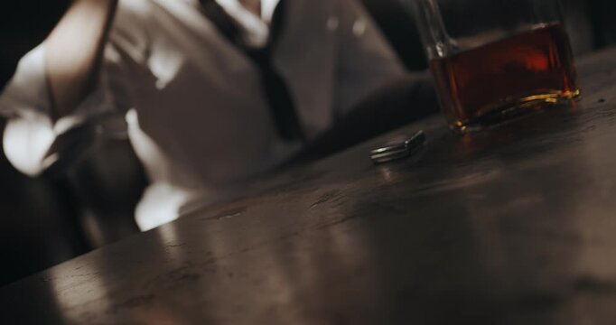 Whiskey glass slides across the table toward a seated man who catches it and takes a drink.