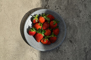 Fresh ripe strawberries on the little grey or gray plate, close up view. background. red. green leaves, leaf. health. sunlight, sunshine. black, dark, shadows. side. front. cement. white wall. half © Muhammad