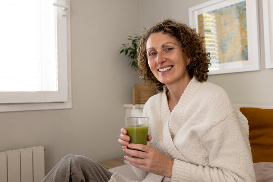 Woman smiling holding green juice in bed