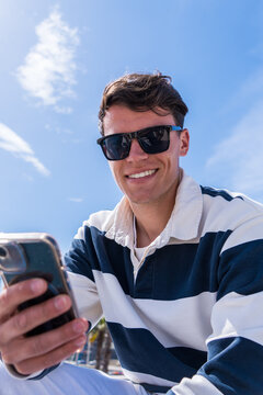 Vertical photo of a young caucasian man holding his phone and look smiling at the camera