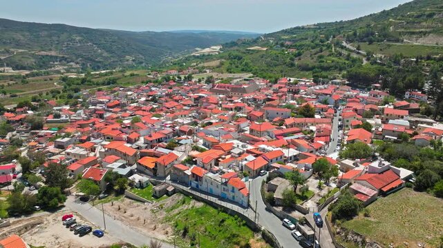 Wide drone view of Omodos village in Cyprus. The red-roofed settlement sits among rolling hills and vineyards, creating a beautiful mountain village panorama.