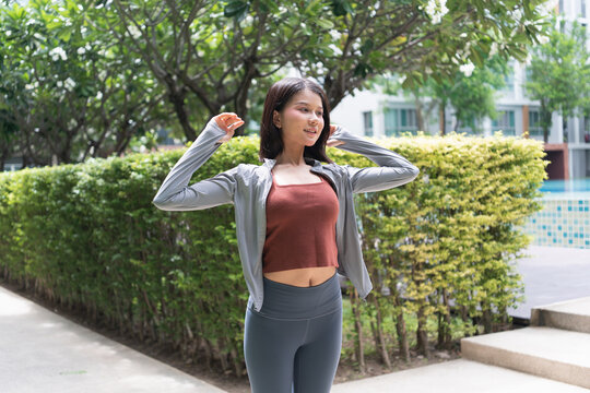 Asian woman stretching before exercise in green urban park feeling refreshed for wellness and healthy lifestyle.