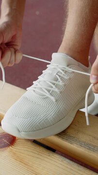 Athlete tying shoelaces before a workout. Tying a white sneaker on a bench close up. Man tying shoelaces on his sport shoes for training outdoors.