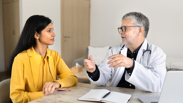 Male doctor consulting woman patient during appointment in clinic office, answering questions, discussing treatment, explain diagnosis, providing professional medical health recommendation and advice