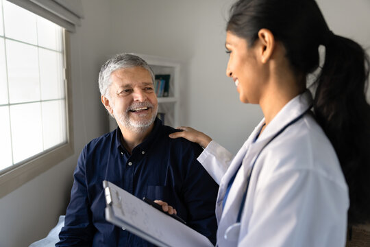 Female doctor holding medical form clipboard, consulting smiling man in clinic office, representing healthcare professional providing health care, wellness services. Patient satisfaction and trust