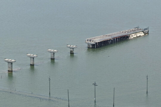 Aerial view of bridge construction showing concrete pillars and a partially completed deck extending over the water in Kishoreganj, Dhaka Division, Bangladesh.