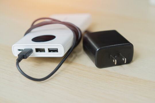 Power bank connected with a USB charging cable resting next to a black wall adapter plug