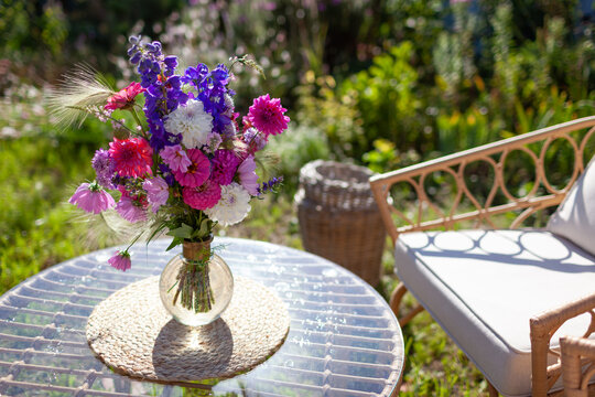 Close up of flower arrangement put on glass table in summer garden. Lounge zone with furniture and bouquet of fresh blooms in vase