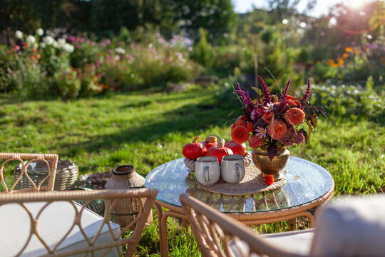 Cozy outdoor spot with furniture in autumnal garden. Table arranged with bouquet of fall flowers, orange pumpkins and coffee 