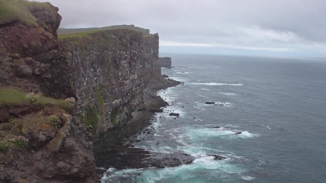 Latrabjarg sea cliffs and North Atlantic coastline in Iceland under overcast skies, puffins fly as small specks