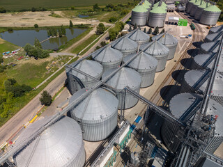 Elevated panoramic viewpoint of large scale industrial grain storage facility showcasing circular metallic silos conveyor pipelines and countryside landscape. © Pasha