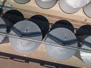 Straight down view of modern agricultural grain storage plant showcasing circular metallic silo structures with shadows cast on concrete ground. © Pasha