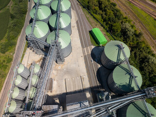 Straight down view of modern agricultural grain terminal showcasing circular metal silos with green roofs and complex transportation tracks. © Pasha