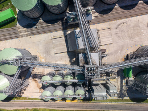 Straight down viewpoint of complex agroindustrial grain elevator plant showing metal processing structures, conveyor bridges, and silos.