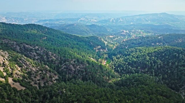 Drone view from Mount Olympus in Cyprus. Green valleys, forested hills and distant mountain ranges create a wide panoramic nature scene.
