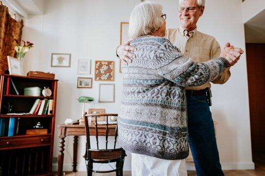 Elderly couple dancing in a cozy living room, surrounded by decor.