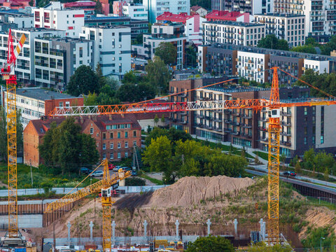 Aerial view of a construction site with multiple tower cranes and excavation work surrounded by modern residential buildings and historic brick architecture in Vilnius, Vilnius County, Lithuania.