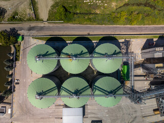 Straight down viewpoint of six circular metal grain silos with vibrant green tops arranged symmetrically at industrial terminal. © Pasha