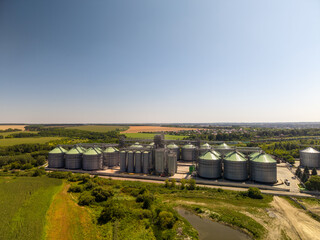 Panoramic high angle view of large scale industrial grain storage terminal with metal silos surrounded by green countryside. © Pasha