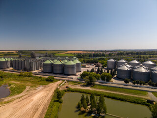 Elevated view of modern agricultural grain elevator complex with metallic silos and processing systems built next to countryside ponds. © Pasha