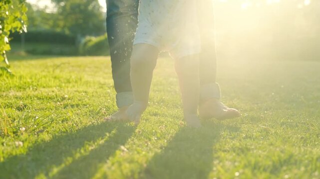 Walking children's bare feet on a green lawn close-up. Child  learns to take the first steps.  Baby learns to walk with the help of his mother on a green grass in the park. Real time 4k video.