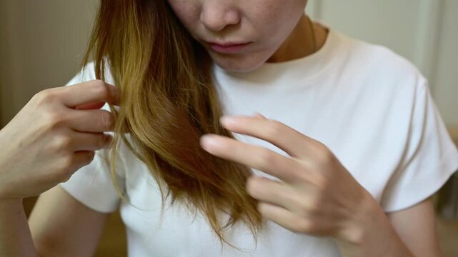 Asian woman holding and checking her damaged split ended hair. Hair damage is risk for further damage and breakage. It may also look dull or frizzy and be difficult to manage.